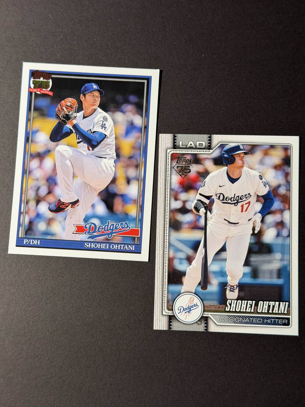 Phone photo of two Shohei Ohtani Topps baseball trading cards lying at an angle on dark cloth, before CardMagic processing